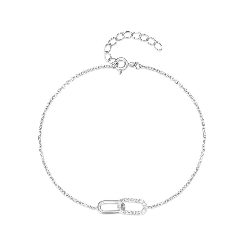 A wrist adorned with a sleek cross-clasp bracelet crafted from polished S925 sterling silver, featuring sparkling cubic zirconia stones embedded in a minimalist dual-buckle design. The bracelet pairs effortlessly with both professional attire and casual outfits, offering a subtle yet refined statement for daily wear.