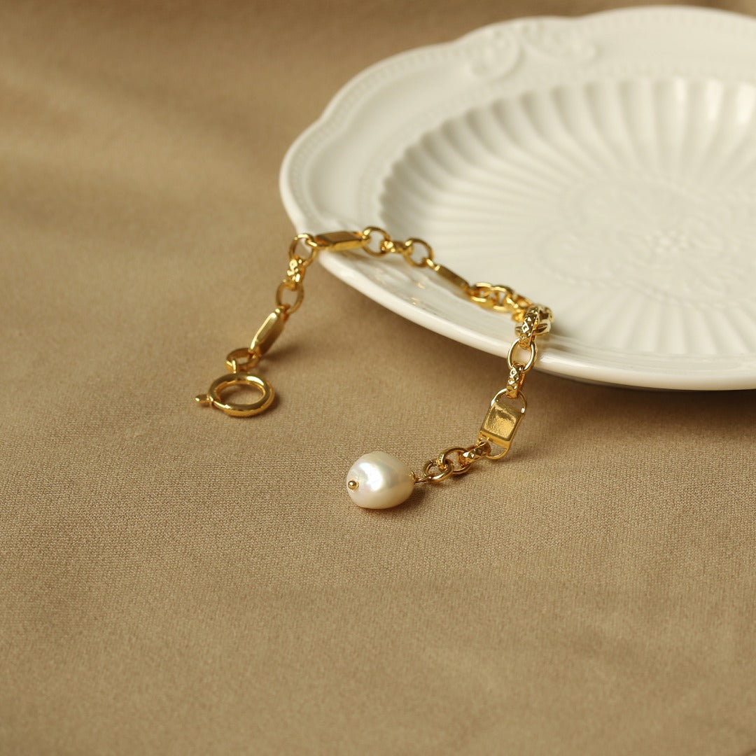 This image showcases an elegant pearl pendant bracelet featuring a delicate gold-tone chain and a lustrous natural pearl centerpiece. Designed for effortless sophistication, this bracelet is perfect for daily wear, evening events, and layering with other jewelry pieces. The timeless combination of a refined gold chain and a radiant pearl makes it an exquisite addition to any jewelry collection, offering both vintage charm and modern elegance.