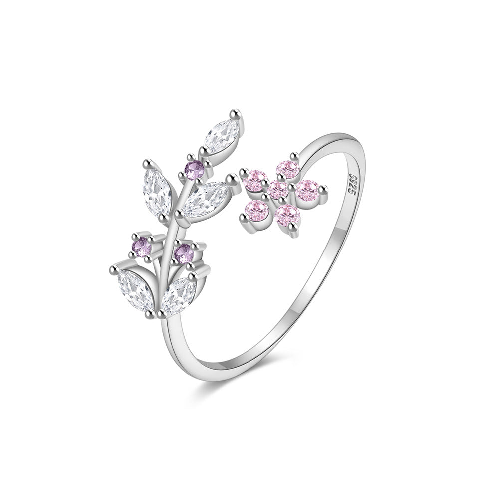 A hand adorned with a nature-inspired open ring featuring delicate silver leaves and pink floral accents with marquise-cut zirconia centers, styled against blooming peonies for a spring garden party photoshoot. The organic design transitions seamlessly from daytime brunch outfits to evening cocktail attire.